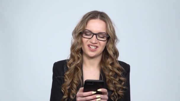 Dissatisfied businesswoman texting on her phone on gray background in studio, slow motion — Stock Video