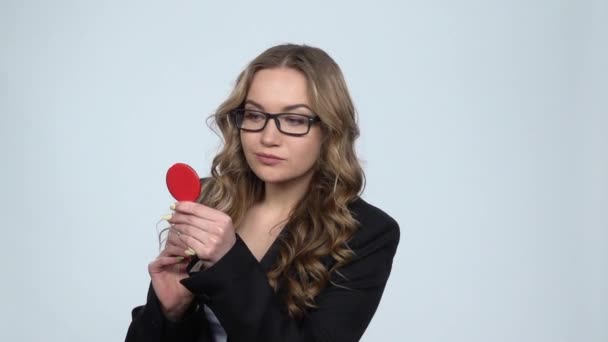 Belle fille en lunettes peint ses lèvres en regardant dans un miroir rouge, au ralenti — Video