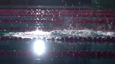 Erkek yüzücü başlangıç blok kapalı atlar ve havuzda yüzmeye başlar. Profesyonel atlet eğitimi: dalış ve su yüzeyi sıçramaları. Gece çekimi