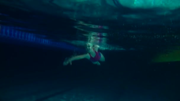 Amateurschwimmer beim Üben im Wasserbecken. Schwimmerin übt Purzelbaum. Unterwasserblick. Nachtschuss — Stockvideo