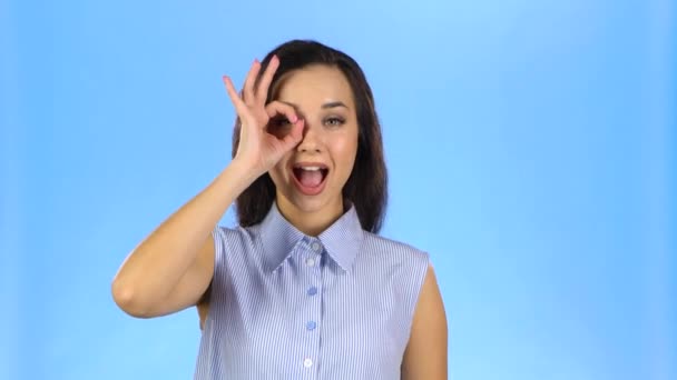 Mujer joven haciendo gesto OK mirando a través de los dedos y guiñando un ojo — Vídeo de stock