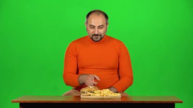 Fazla kilolu beyaz bir adam hamburger ve patates kızartması yemek istiyor, sağlıksız yemek ama bir elma seç, yeşil ekran.