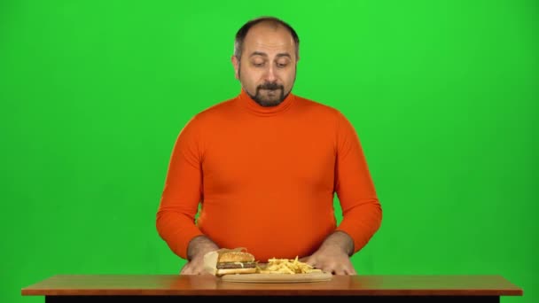 Чоловік з надмірною вагою дивиться на смачні нездорові продукти на столі і хоче з'їсти його, зелений екран — стокове відео