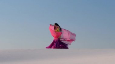 Kumlu çölde pembe peçeli profesyonel bir dansçı.