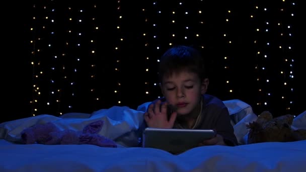 Child is lying on a bed holding a laptop and watching a cartoon. Bokeh background. Slow motion — Stock Video