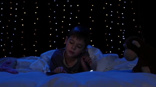 Little boy at night reading a book on the bed. Bokeh background. Slow motion — Stock Video