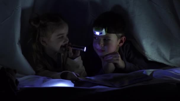 Kisgyerekek a takaró alatt, világítsatok egymásra egy zseblámpával. Lassú mozgás. — Stock videók