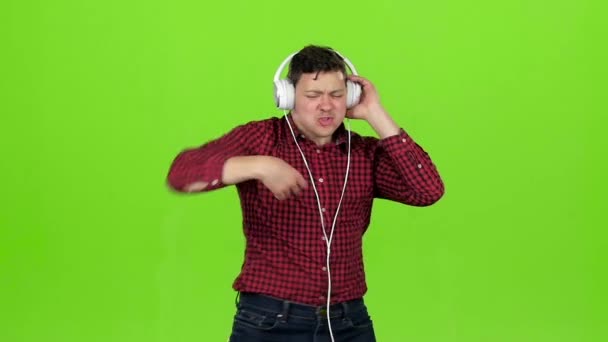 Guy escucha música enérgica en auriculares y bailes. Pantalla verde. Movimiento lento — Vídeos de Stock