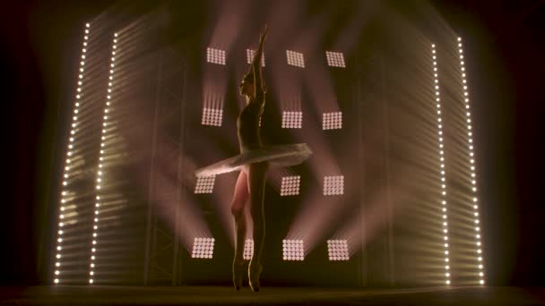 Sahne ışıkları altında dans eden profesyonel balerin büyük sahnede sigara içiyor. Sahne ışıkları altında beyaz etek giyen güzel bir kız. — Stok video