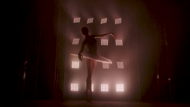 Bailarina de silueta elegante bailando en vestido negro en el estudio en el centro de atención en el escenario del teatro. Bailarina de ballet diligente interpretando elementos de baile del ballet clásico. Movimiento lento . — Vídeos de Stock