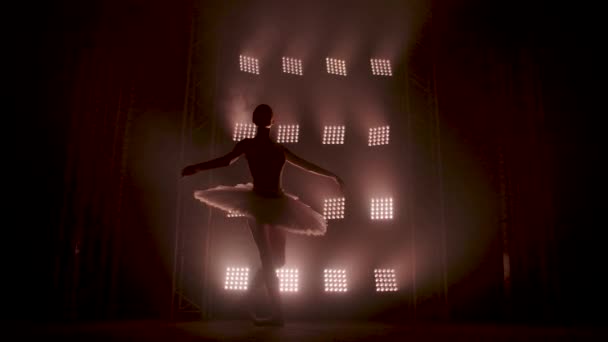 Graceful silhouette ballerina dancing in black dress in the studio in spotlight on the stage of the theater. Diligent ballet dancer performing dancing elements of classical ballet. Slow motion. — Stock Video