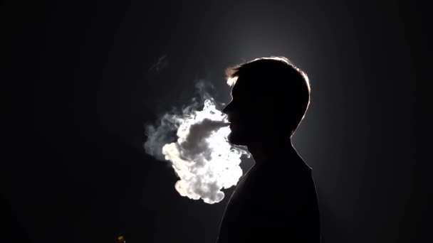 Profile view silhouette bearded man blowes thick smoke when smoking hookah on black background in slow motion, close up — Stock Video