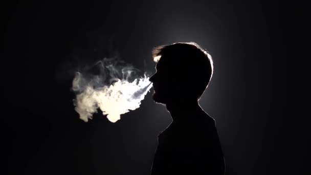 Profile view of silhouette bearded man blowes smoke through the nose in slow motion on black background, close-up — Stock Video