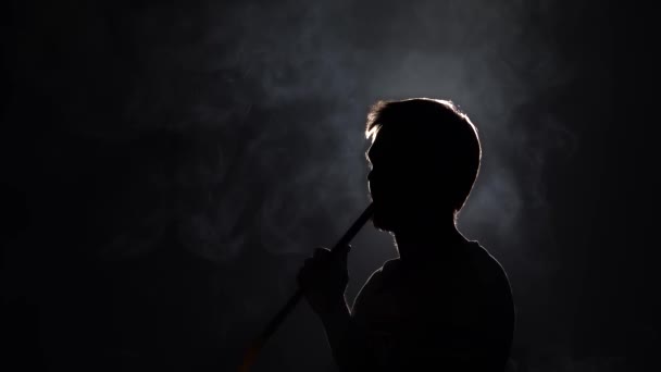 Silhouette di uomo barbuto soffia fumo quando si fuma narghilè su sfondo nero al rallentatore. Primo piano, vista profilo. — Video Stock