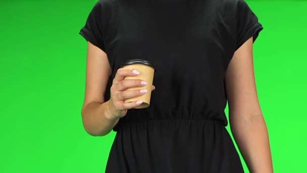 Feminino bebendo café enquanto caminha, de perto. Menina com cabelo loiro em um vestido preto em uma tela verde. Movimento lento . — Vídeo de Stock