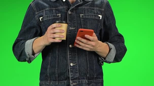 손에 붉은 핸드폰을 들고 걷는 동안 커피를 마시는 남자. 녹색 화면. 느린 동작 — 비디오