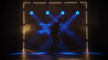 Yetenekli genç bir hip hop dansçısının silueti. Karanlık bir stüdyoda, dumanlı ve neon ışıklı bir sahnede hip hop sokak dansı. Dinamik ışıklandırma efektleri. Yaratıcı yetenekler. Yavaş çekim.