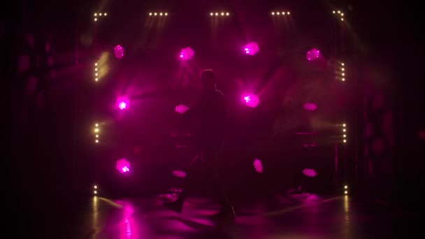 Silhouette of a talented young hip hop dancer. Hip hop street dance on a stage in dark studio with smoke and neon lighting. Dynamic lighting effects. Creative skills. Slow motion. — Stock Video