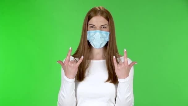 Πορτρέτο του όμορφου κοριτσιού σε ιατρική προστατευτική μάσκα προσώπου κοιτάζοντας κάμερα και κάνοντας μια ροκ χειρονομία με τα δύο χέρια. — Αρχείο Βίντεο