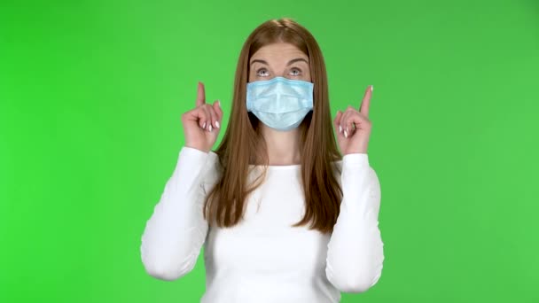 Retrato de menina bonita em máscara protetora médica olhando para a câmera e apontando os dedos . — Vídeo de Stock