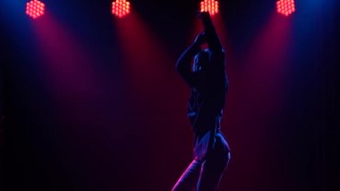 Yetenekli genç bir hip hop dansçısının silueti. Karanlık bir stüdyoda, dumanlı ve neon ışıklı bir sahnede hip hop sokak dansı. Dinamik ışıklandırma efektleri. Yaratıcı yetenekler. Yavaş çekim.