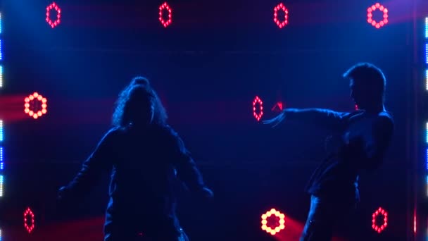 Silhouettes d'une jeune fille et d'un garçon talentueux danseurs hip hop. Danse de rue hip hop sur une scène dans un studio sombre avec de la fumée et un éclairage au néon. Effet d'éclairage dynamique. Des talents créatifs. Mouvement lent. — Video