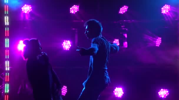 Silhouettes of a talented young girl and boy hip hop dancers. Hip hop street dance on a stage in dark studio with smoke and neon lighting. Dynamic lighting effects. Creative skills. Slow motion. — Stock Video