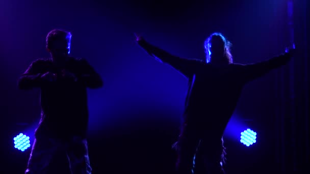 Silhouetten van een getalenteerd jong meisje en jongen hip hop dansers. Hip hop straat dans op een podium in donkere studio met rook en neon verlichting. Dynamische lichteffecten. Creatieve vaardigheden. Langzame beweging. — Stockvideo