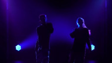 Yetenekli genç bir kız ve oğlanın siluetleri hip hop dansçıları. Karanlık bir stüdyoda, dumanlı ve neon ışıklı bir sahnede hip hop sokak dansı. Dinamik ışıklandırma efektleri. Yaratıcı beceriler.
