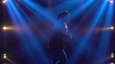 Yetenekli genç bir hip hop dansçısının silueti. Karanlık bir stüdyoda, dumanlı ve neon ışıklı bir sahnede hip hop sokak dansı. Dinamik ışıklandırma efektleri. Yaratıcı beceriler.