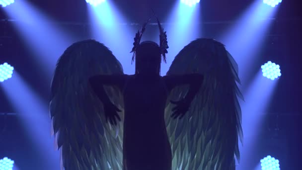 Silhuett av dansande grekiska gudinnan Artemis med vingar på scenen i en mörk studio med rök och neonljus. Ljusa neonljuseffekter. Lyxig teater prestanda sång och dans show. — Stockvideo
