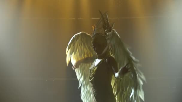 Silhueta de dança grega Deusa Ártemis com asas no palco em um estúdio escuro com fumaça e iluminação de néon. Uma jovem brilhante com um vestido dourado e uma cobertura para a cabeça. Efeitos dinâmicos de iluminação de néon — Vídeo de Stock