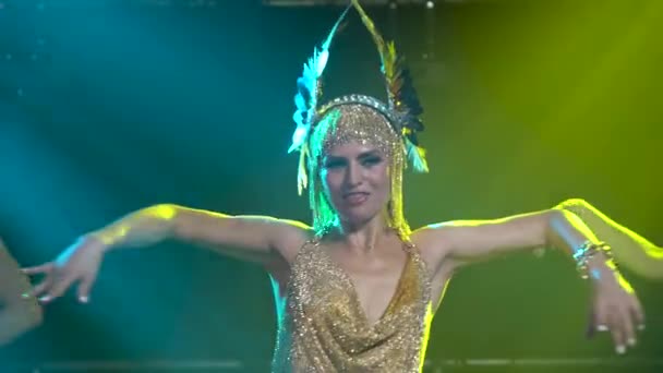 Tänzerische und singende griechische Göttin Artemis auf der Bühne in einem dunklen Studio mit Rauch und Neonlicht. Eine helle junge Frau in goldenem Kleid und Kopfbedeckung. Dynamische Neonlichteffekte. Luxuriös — Stockvideo
