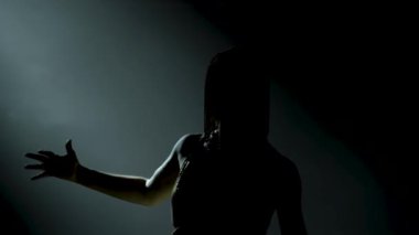 Dans eden Yunan Tanrıçası Artemis 'in silueti dumanlı ve neon ışıklı karanlık bir stüdyoda sahnede. Altın elbiseli ve başlıklı, kılıçlı, parlak, genç bir kadın. Dinamik neon ışıklandırma efektleri