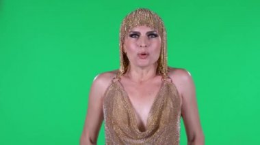 Güzel genç kadınların portresi şaşırmış ve şaşırmış bir ifadeyle dimdik ayakta duruyor. Stüdyoda yeşil bir ekranda parlak bir makyaj elbisesi ve başlık..