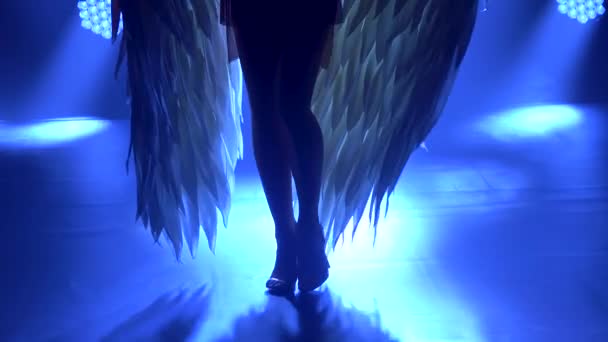 煙とネオンの照明と暗いスタジオでステージ上でギリシャの女神アルテミスを踊るのシルエット.金色のドレスと頭飾りの翼を持つ明るい若い女性。ダイナミックなネオン照明効果 — ストック動画