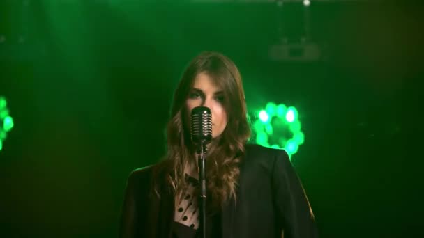 Güzel bir vokal kız klasik bir mikrofonla sahneye yaklaşır. Siyah bir elbise ve omuzlarında erkek ceketi ve dudaklarında kırmızı ruj. Dumanlı karanlık stüdyo ve — Stok video