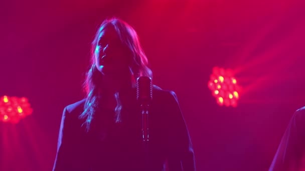 Silhouette una hermosa cantante cantando bailes y gestos con sus manos en el escenario en un micrófono vintage. Estudio oscuro con humo e iluminación de neón. Efectos dinámicos de iluminación de neón. Rendimiento — Vídeo de stock