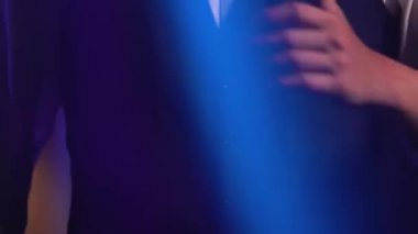 Genç stil sahibi bir vokalist elleri klasik bir mikrofonda sahnede şarkı söylüyor ve jestler yapıyor. Dumanlı ve neon ışıklı karanlık stüdyo. Dinamik neon ışık efektleri. Performans vokal ve