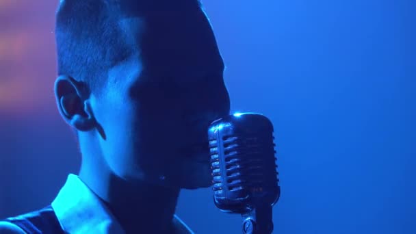 Silhouette ein junger stylischer Kerl Sänger emotional singt und gestikuliert mit den Händen auf der Bühne in einem Vintage-Mikrofon. Dunkles Studio mit Rauch und Neonlicht. Dynamische Neonlichteffekte — Stockvideo