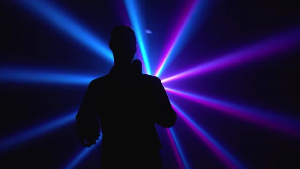 Silhouette un jeune chanteur chic chantant émotionnellement et gestes avec ses mains sur scène dans un microphone vintage. Studio sombre avec fumée et néon. Effet lumineux néon dynamique