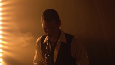 Siluet, genç ve şık bir adam sahnede altın gibi parlak bir saksafon çalıyor. Dumanlı ve neon ışıklı karanlık stüdyo. Performans vokali ve müzik grubu. Kapat..