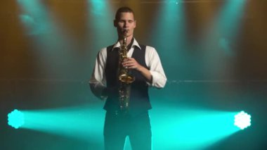 Genç, modaya uygun bir adam, sahnedeki turkuaz spot ışıklarıyla altın gibi parlak bir saksafonda çalar. Dumanlı ve neon ışıklı karanlık stüdyo.