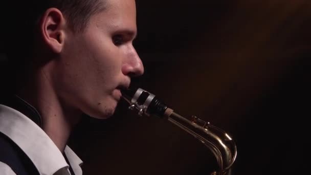 Un joven retro con estilo juega en el saxofón dorado brillante en el escenario. Estudio oscuro con humo e iluminación de neón. Las manos y el saxofón de cerca. Vista lateral. — Vídeos de Stock