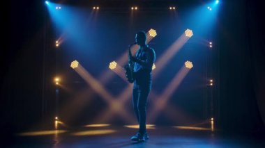 Siluet genç ve şık bir adam sahnede parlak spot ışıklarıyla saksafon çalıyor. Dumanlı ve neon ışıklı karanlık stüdyo. Dinamik neon ışık efektleri. Performans vokali ve müzik grubu. Yavaş