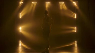 Siluet, genç ve şık bir adam sahnedeki sarı spot ışıklarında altın gibi parlak bir saksafon çalıyor. Dumanlı ve neon ışıklı karanlık stüdyo. Performans vokali ve müzik grubu. Yavaş çekim.
