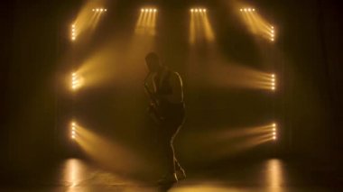 Siluet, genç ve şık bir adam sahnedeki sarı spot ışıklarında altın gibi parlak bir saksafon çalıyor. Dumanlı ve neon ışıklı karanlık stüdyo. Performans vokali ve müzik grubu. Yavaş çekim.