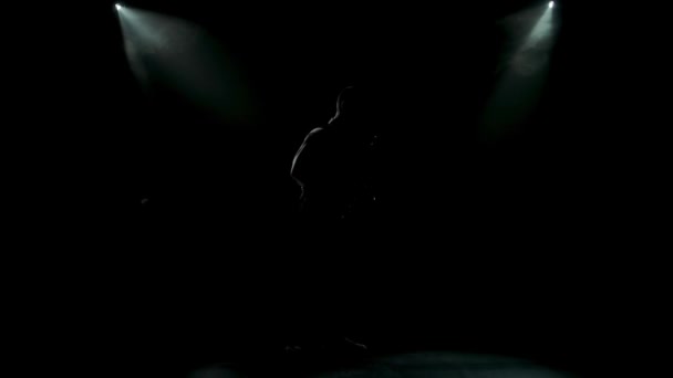 Silhouette un giovane ragazzo elegante suona il sassofono dorato lucido sotto i riflettori gialli sul palco. Studio scuro con fumo e luci al neon. Performance vocale e banda musicale. Vista laterale. Rallentatore. — Video Stock