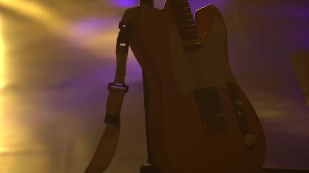 Elektrická kytara na jevišti v jasném neonovém světle. Tmavé studio s kouřem a dynamickými neonovými světelnými efekty. Natáčení zdola nahoru. Zavřít. — Stock video