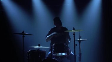 Karanlık bir stüdyoda, dumanlı ve neon ışıklı davul setinde davul çalan siluet davulcusu. Performans vokali ve müzik grubu. Yakın plan..